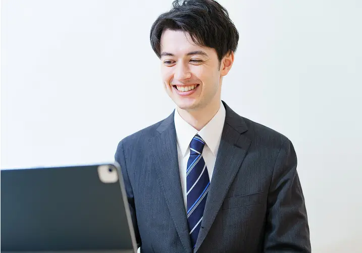 スーツ姿の男性がパソコン画面を見ながら笑顔でオンライン会議をしているシーン
