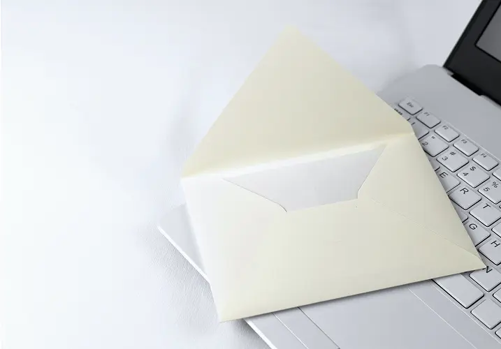 ノートパソコンの上に白い封筒が置かれ、メールやメッセージを象徴するイメージ